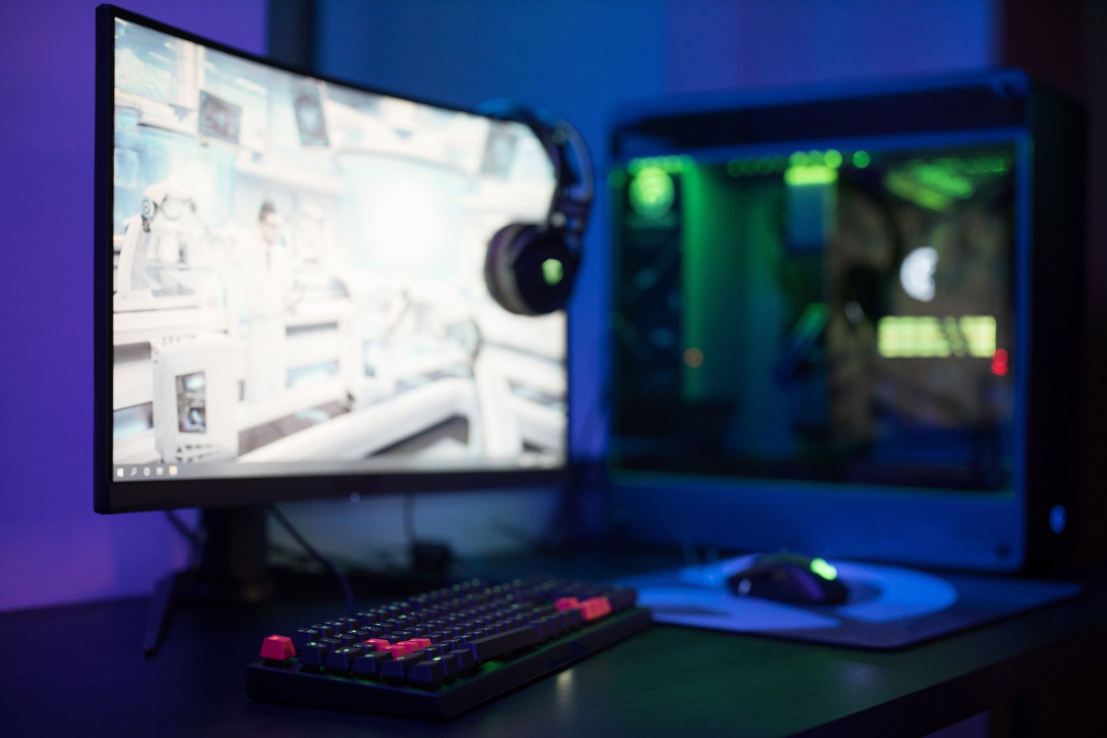Curved monitor, headphones and gaming PC lit in blue and green