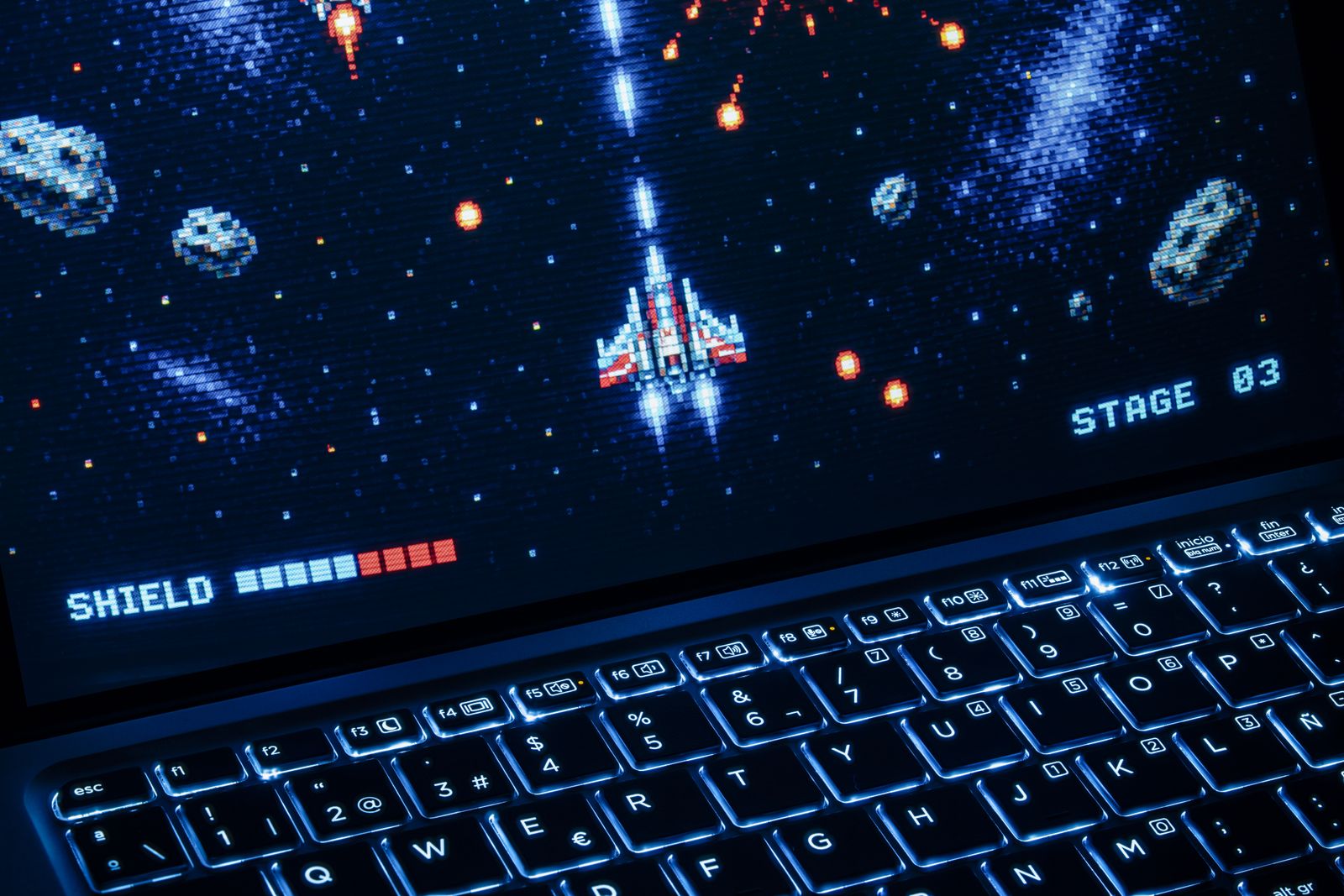 Retro pixel-art space shooter running on a laptop with a backlit keyboard