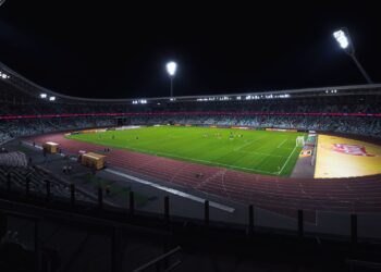Football stadium at night with floodlights on and players warming up on the pitch
